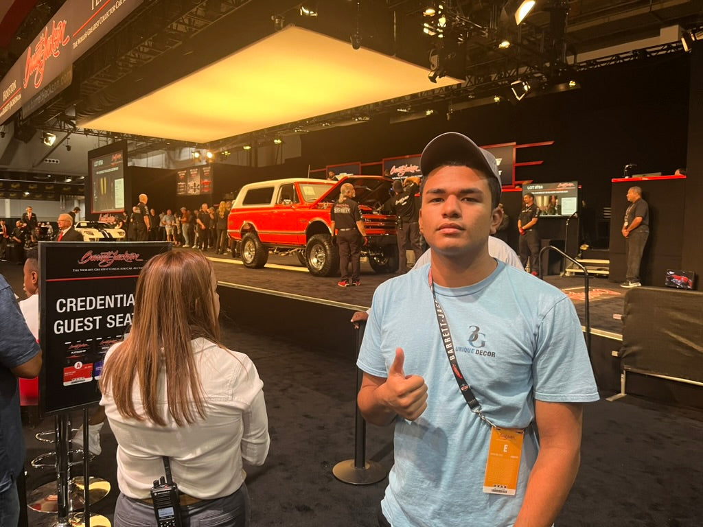 3G Unique Decor booth at Barrett-Jackson featuring handcrafted automotive decor including piston lamps, turbo lamp, and NASCAR tire table on the vendor floor.
