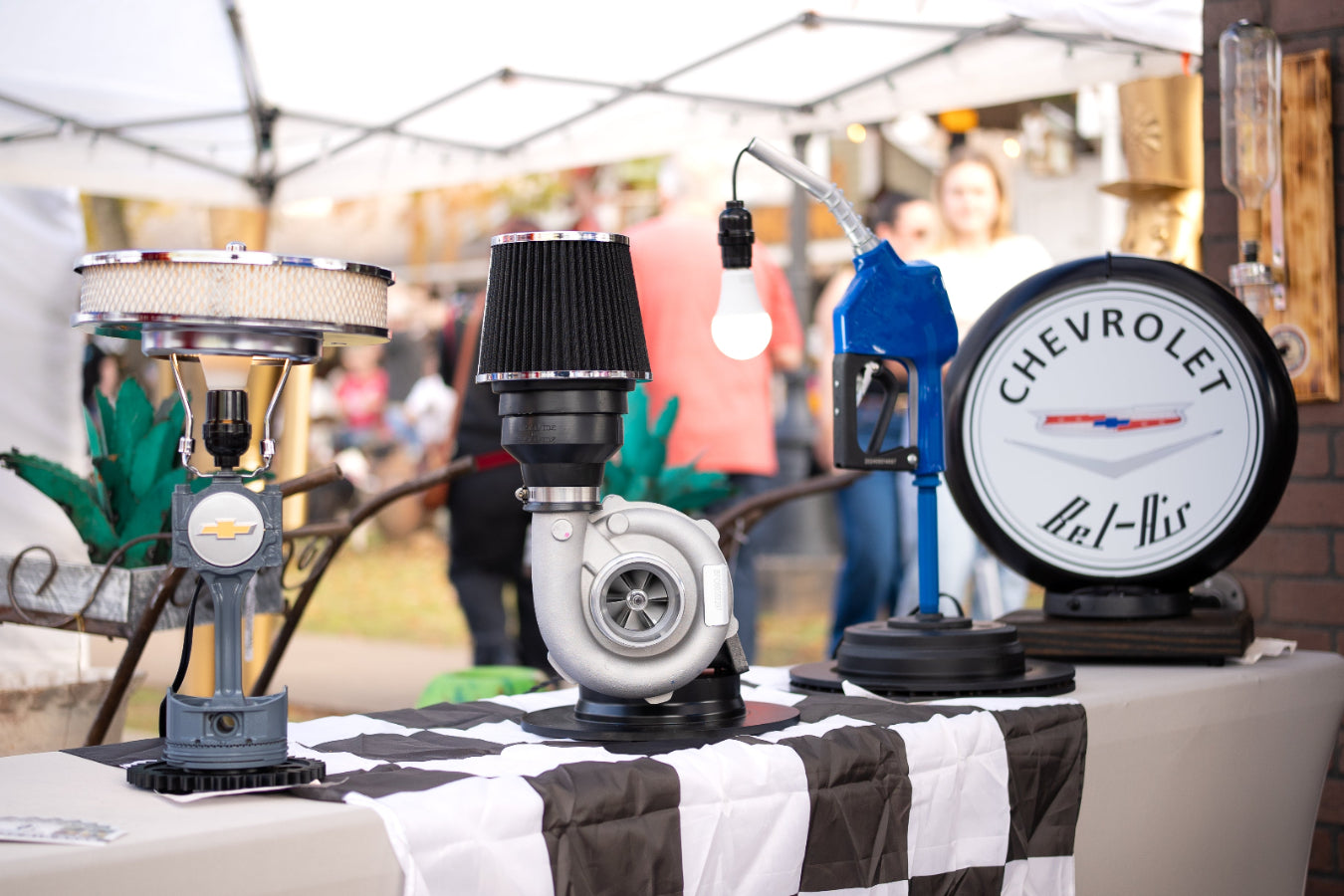 3G Unique Decor booth display at Tomball German Fest featuring handcrafted piston lamps, a turbo lamp, gas pump light, and Chevrolet sign.