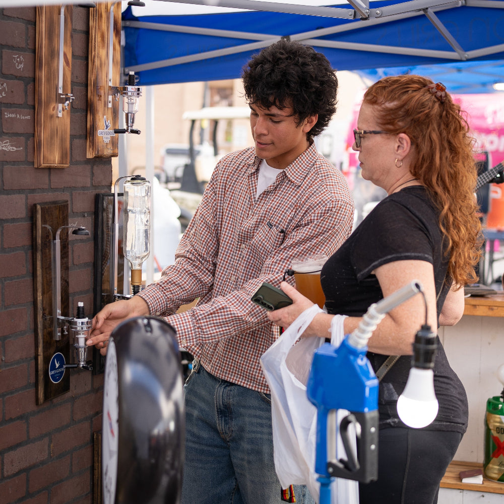 Customer testing a wall-mounted liquor dispenser product at the 3G Unique Decor booth during Tomball German Fest.