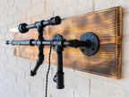 Wall-mounted light fixture with black pipes and wooden panel on a brick wall.