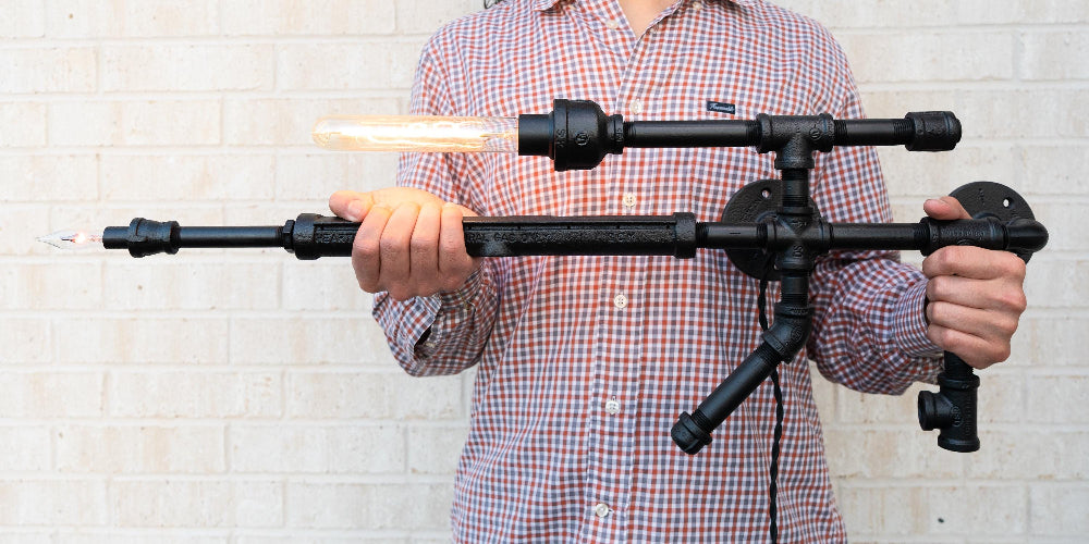 Person holding a black metal tripod against a white brick wall.
