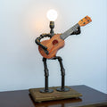 Ukulele-shaped lamp with metal stand on a wooden base against a light blue wall.