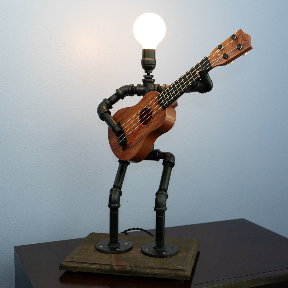 Ukulele lamp with metal legs on a wooden base against a light blue wall.