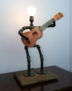 Ukulele lamp with black metal frame on a wooden base against a light blue wall.
