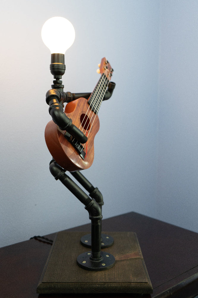 Guitar-shaped lamp with light bulb on a wooden base against a plain background