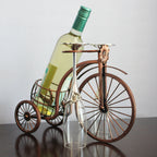Wine bottle holder shaped like a vintage bicycle with a wine bottle and glass on a plain background