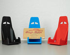 Three car seat models in black, blue, and red with a cardboard sign in the center on a white surface.