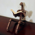 Pipe sculpture with a light bulb head reading a book on a wooden surface.