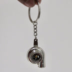 Metal keychain shaped like a turbocharger on a plain background