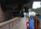 Close-up of a valve with a carabiner attached, set against a blurred outdoor background.