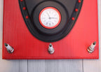 Red clock with black border and white face on a wooden surface