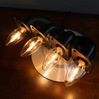 Handcrafted automotive desk lamp made from a black 4-cylinder exhaust manifold with four warm lit candle flame bulbs on a metal base.